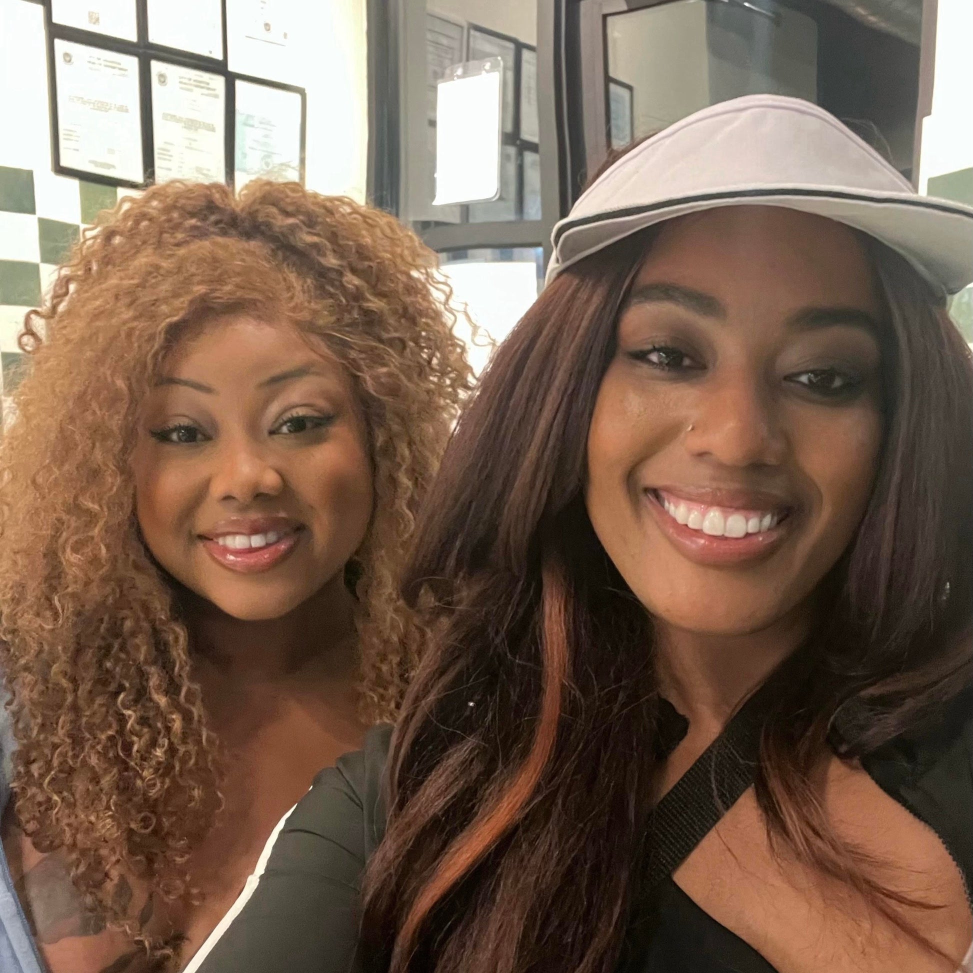 Two women taking a selfie in front of a glass door. On left woman is wearing blonde curly hair by Seksi Hair.