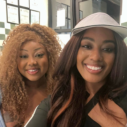 Two women taking a selfie in front of a glass door. On left woman is wearing blonde curly hair by Seksi Hair. 